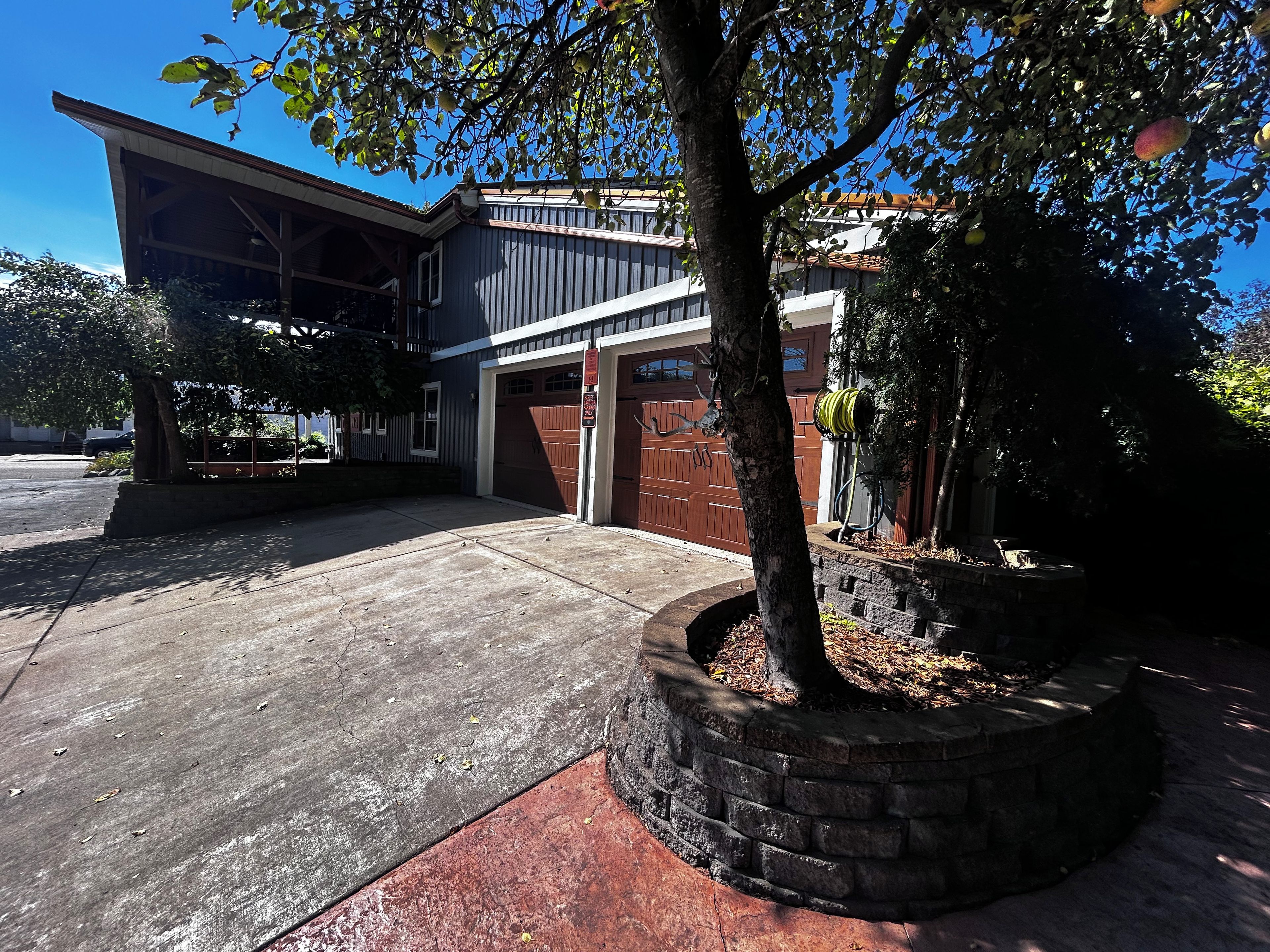 Una propiedad residencial con garaje, un porche cubierto y un área ajardinada con un árbol.