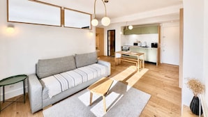 A modern living room with a sofa, a coffee table, and a dining area with a table and chairs. There is a kitchen in the background with cabinets and appliances. - Ersextius, LMR1, Aix-en-Provence (Aix-en-Provence)