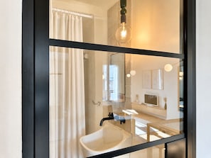 Une salle de bain moderne avec une paroi de séparation en verre, un lavabo blanc et un rideau de douche.