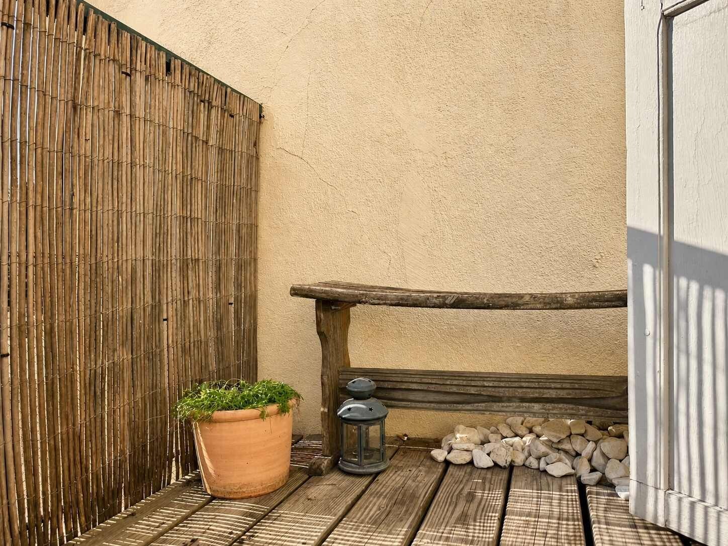 Un banc en bois, une plante en pot et une lanterne sur une terrasse en bois.