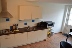 A compact kitchen with a gas stove, a microwave, and a sink. - Holiday apartment with 1 bedroom (Nes Ameland)