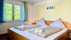 Habitación de hotel con dos camas, una ventana con cortinas, una mesita de noche con lámpara y un cuadro colgado en la pared.