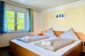 Une chambre d’hôtel avec deux lits, une fenêtre avec des rideaux, une table de chevet avec une lampe et un tableau accroché au mur.