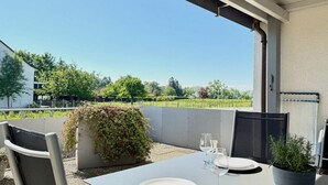 Un área de comedor al aire libre con una mesa preparada para dos personas, una silla y una planta en maceta.