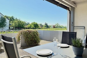 Un espace extérieur aménagé pour prendre les repas, avec une table dressée pour deux personnes, une chaise et un pot de fleurs.