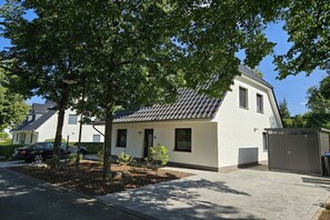 Ein modernes, zweistöckiges Haus mit Ziegeldach, Auffahrt und kleinem Garten.