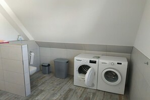 Ein Waschraum mit zwei Waschmaschinen, einem Mülleimer und einer Toilette.