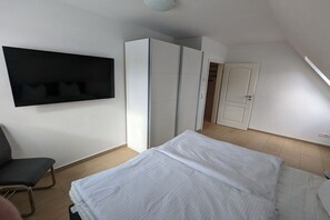 Ein Schlafzimmer mit einem Bett, einem Sessel, einem Kleiderschrank und einem Fernseher an der Wand.