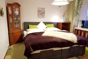 Ein Schlafzimmer mit Bett, Nachttisch, Schrank, Gemälde und Fenster mit Vorhängen.