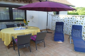 Une terrasse avec une table dressée pour deux personnes, deux chaises, un parasol violet et un mur en treillis blanc.