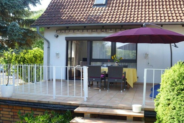 Ein Haus mit überdachter Terrasse, einem Esstisch und Stühlen sowie einem großen Sonnenschirm.