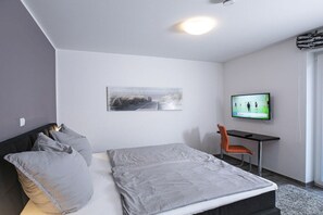 Una camera da letto moderna con un letto, una scrivania, una sedia, un televisore e un quadro appeso al muro.