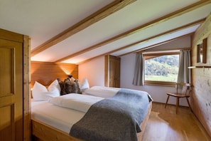 Ein Schlafzimmer mit Holzbalkendecke, einem Bett mit weißer Bettwäsche, einer grauen Decke und einem Fenster mit Blick ins Freie.