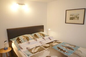 Ein Schlafzimmer mit einem Bett, einer Nachttischlampe, einem gerahmten Bild an der Wand und einer Wandleuchte.