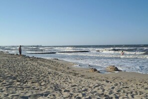 Ein Strand mit Sand, Wellen und einem Pier in der Ferne.