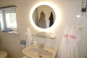 Ein Badezimmer mit rundem Spiegel, Waschbecken und Fenster.