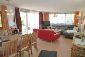 En stue med en rød sofa, en grå sofa, træstole, et spisebord og et fjernsyn.