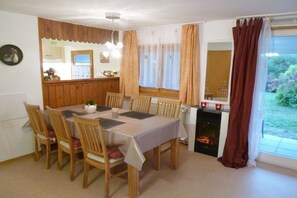 Ein Essbereich mit einem Tisch für vier Personen, Holzstühlen, einem Kamin und Blick ins Freie.