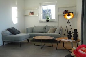 A modern living room with a grey sofa, two round coffee tables, a floor lamp, and a window with a view of trees. - Holiday home with 3 bedrooms (Poseritz OT Mellnitz-Hof)