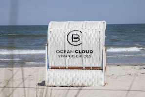 Un asciugamano da spiaggia con la scritta 'OCEAN CLOUD STRANDSCHLOSS', posizionato su una spiaggia sabbiosa con l'oceano sullo sfondo.