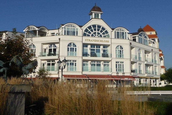 Un grande edificio bianco con la scritta 'STRANDSCHLOSS' ben visibile. Presenta numerose finestre, una cupola centrale e un tetto rosso.