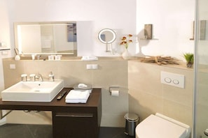 Un bagno moderno con uno specchio grande, un lavandino, un water e una piccola pianta sul ripiano.