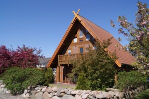 A traditional wooden chalet with a steeply pitched roof, a balcony, and a stone wall surrounding the property. - Dat Fachwerkhus 1.OG (Ostseebad Trassenheide)