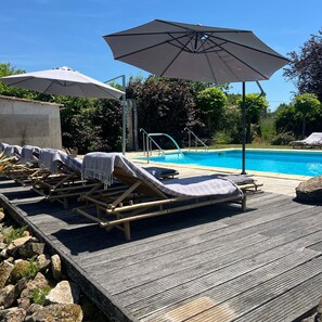 A poolside area with lounge chairs and umbrellas, a pool, and a wooden deck.