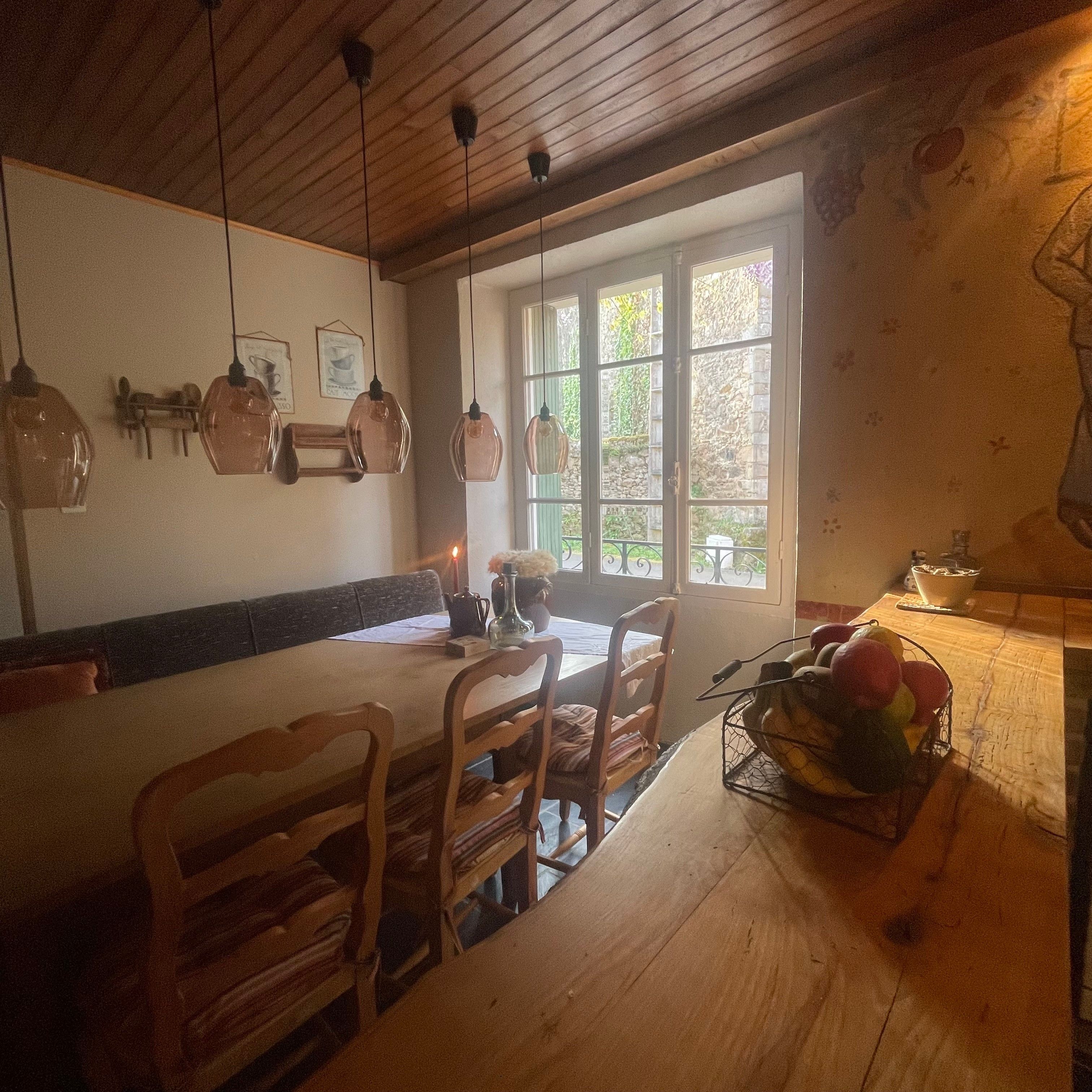 Una mesa de comedor de madera con sillas, lámparas colgantes y un ventanal con vistas al verdor.