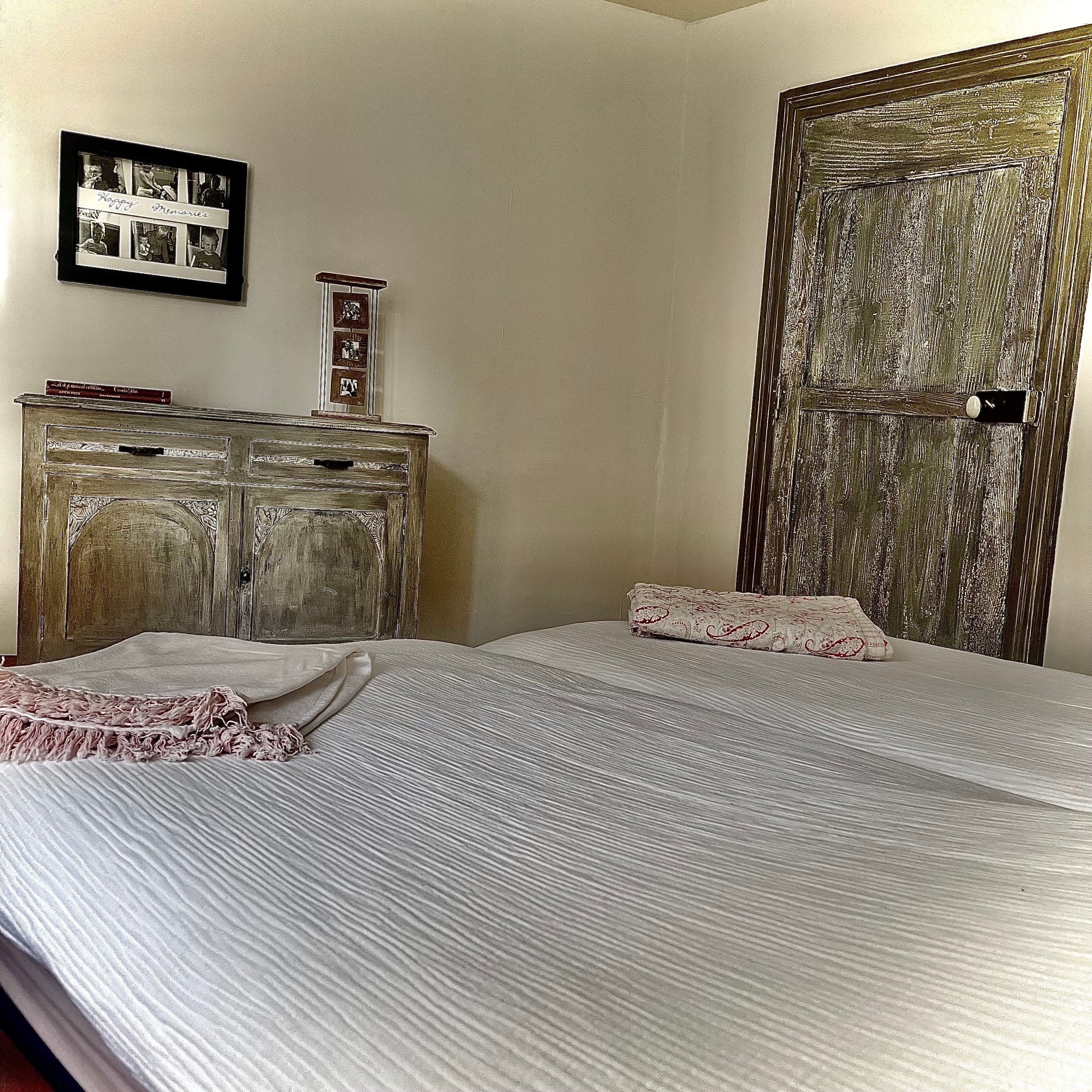 A bedroom with two beds, a dresser, and a door.