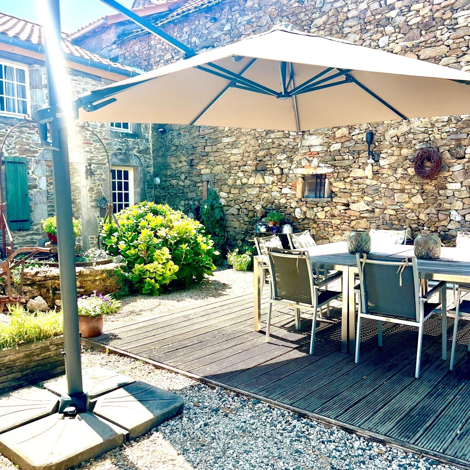 Een terras met een tafel en stoelen, een stenen muur en een pergola met een parasol.