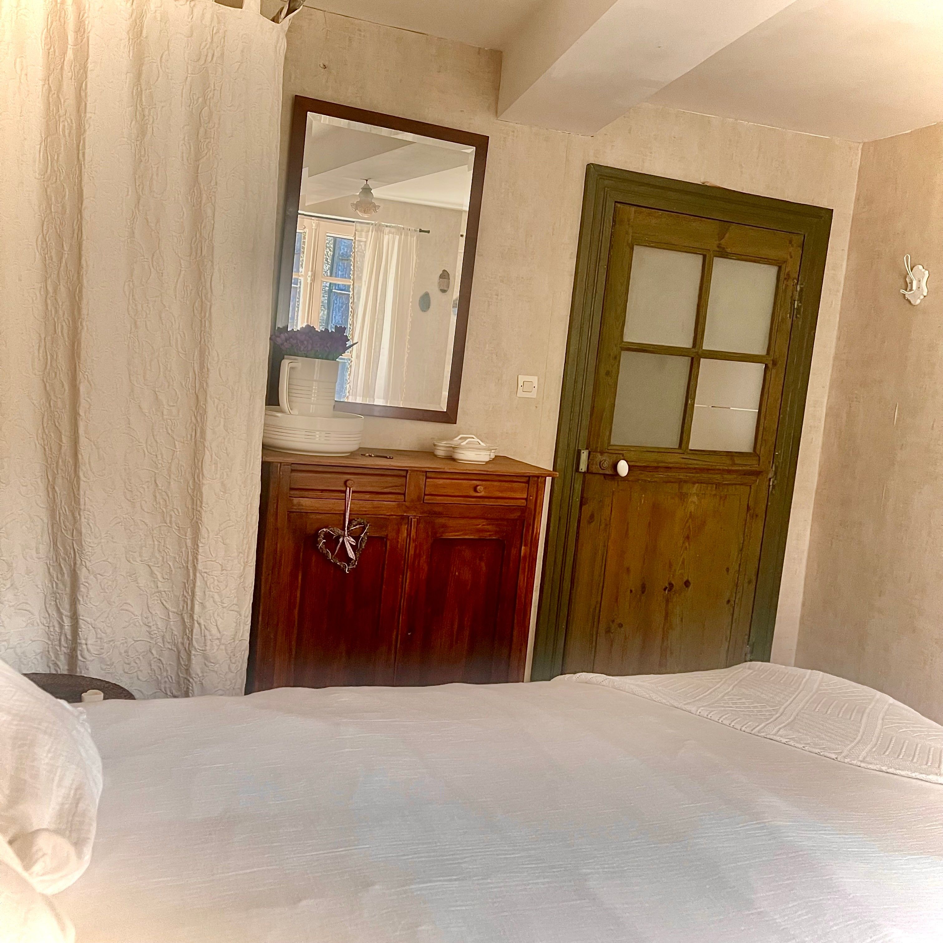 Una habitación con una cama, un aparador de madera, un espejo y una puerta verde.