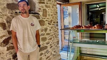 Un homme se tient dans un couloir aux murs de pierre, devant une vitrine de boulangerie remplie de pâtisseries.