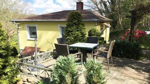 Ein gelbes Haus mit Schornstein, einem Tisch mit Stühlen und einem Garten mit verschiedenen Pflanzen und Blumen.