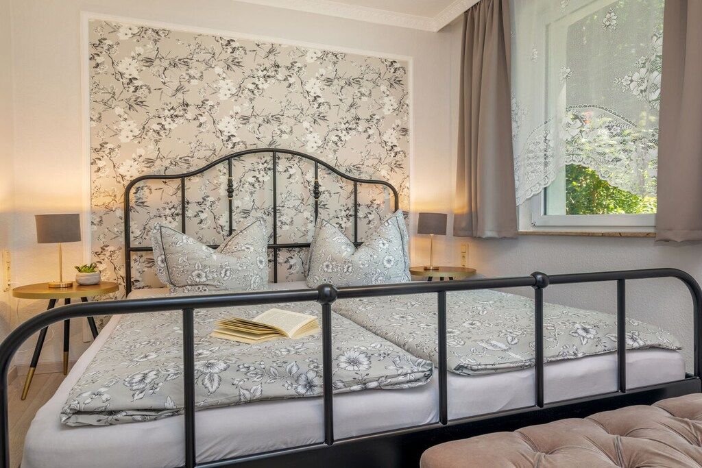 A bedroom with a bed, a nightstand, a window with curtains, and a view of greenery outside.