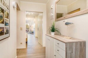 A hallway with a wooden floor, a white cabinet with drawers, a potted plant, a wall-mounted mirror, and a framed picture collection. - Beach bliss at the Baltic Sea House (Binz)