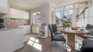 Une cuisine moderne avec des meubles blancs, un îlot central doté d’une planche à découper et un coin repas avec une table ronde et des chaises.