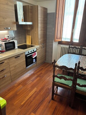 A compact kitchen with wooden cabinets, a microwave, an oven, and a dining table with chairs. - House of the Hoopoe (Firenze)