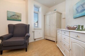 Ein Zimmer mit grauem Sessel, einem weißen Schrank und Kunstwerken an den Wänden.