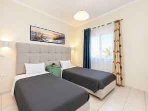 Habitación de hotel con dos camas, un cuadro en la pared, una ventana con cortinas y una mesita de noche con lámpara.