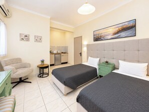 Habitación de hotel con dos camas, un escritorio, una silla, kitchenette y un cuadro en la pared.