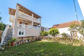 A multi-story building with a balcony, a staircase, and a fenced garden area.