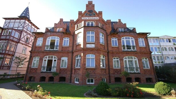 Un grand bâtiment en briques rouges, doté de nombreuses fenêtres et d’une enseigne sur laquelle on peut lire « Villa Gluckspilz ».