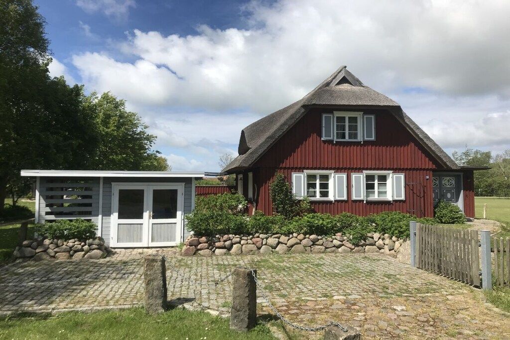 Une maison rouge avec une porte blanche et des volets aux fenêtres, un mur de pierre et une clôture en bois.