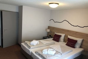 Ein Hotelzimmer mit zwei Betten, einem hölzernen Kopfteil, einem Wandbild, einer Nachttischlampe und einer Tür.
