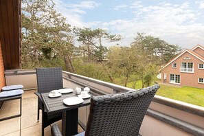 An outdoor dining area with wicker furniture and a table set for two, overlooking a brick house and trees. - Holiday apartment with 1 bedroom (St. Peter-Ording)