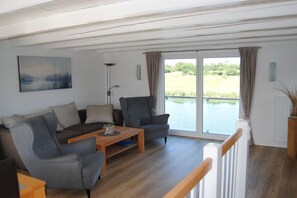 Ein modernes Wohnzimmer mit einer Couch, Sesseln, einem Couchtisch und Blick auf ein Gewässer durch eine Glastür.