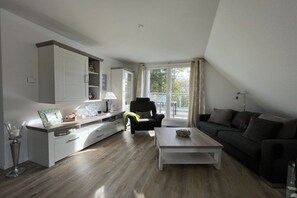 A modern living room with a sofa, a coffee table, and a dining area with a cabinet. - Holiday apartment with 2 bedrooms (Scharbeutz)