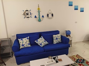A room with a blue sofa, star-patterned cushions, a white coffee table, and wall decorations including a life ring and a welcome sign.
