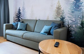A sofa with multiple cushions, a round wooden side table, and a remote control on it. - Kehlstein Apartment, 55 square meters, for 2–4 people (Berchtesgaden)